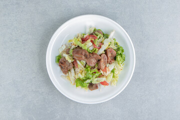 A white plate of fried meat and vegetable salad