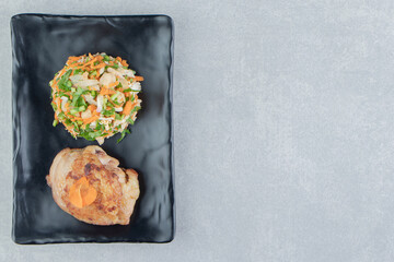 A black plate of chicken fried meat and vegetable salad