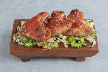 A wooden board with fried chicken legs and vegetable salad