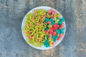 Farfalle and fusilli pasta on the plate, on the marble background
