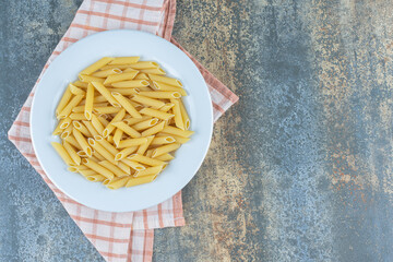 Penne pasta on the plate, on the towel , on the marble background