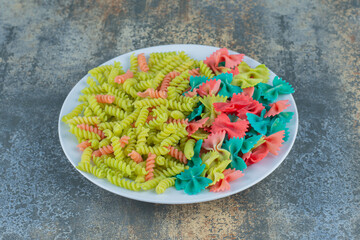 Farfalle and fusilli pasta on the plate, on the marble background