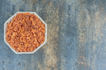 Heart shaped rotelle pasta in the bowl, on the marble background