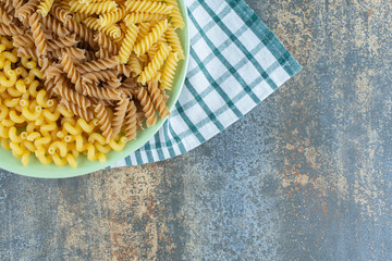 Various pastas in bowl on the towel, on the marble background