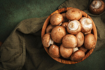 Fresh brown champignon mushrooms in wooden bowl, green stone kitchen table, top view, copy space