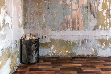 A black trash bag with pieces of paper wallpaper stands in the corner of a room with shabby walls...