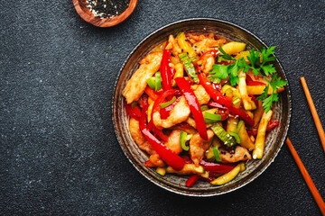 Asian cuisine, stir fry with chicken, red paprika pepper and zucchini bowl. Black kitchen table background, top view, copy space