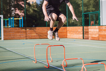 Blond boy in sportswear jumps over red obstacles to improve lower body dynamics. Plyometric...