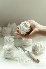 Female confectioner hand hold homemade apple white marshmallow on a white background. Homemade healthy meringue cakes on a parchment sprinkled with powdered sugar