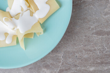 Yogurt on lasagna sheets next to greens on the plate, on the marble background