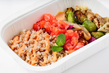 Poke with brown rice, salmon and grilled vegetables in a plastic takeout container