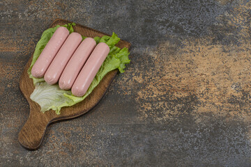 Tasty boiled sausages and lettuce on wooden board