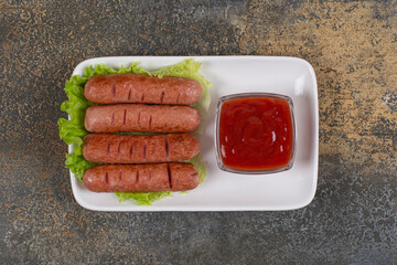 Fried sausages and ketchup on white plate with lettuce