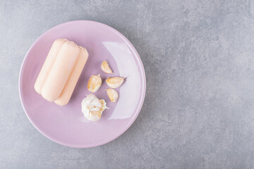 A purple plate of boiled sausages with garlics