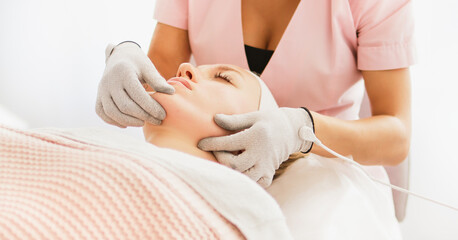 Beautician cosmetologist makes a procedure on the face with microcurrent therapy gloves. Hardware cosmetology in clinic salon for client.	