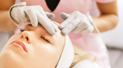 Beautician cosmetologist makes a procedure on the face with microcurrent therapy gloves. Hardware...