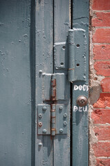 Partial view of an old  blue iron door with three hinges and a door bell
