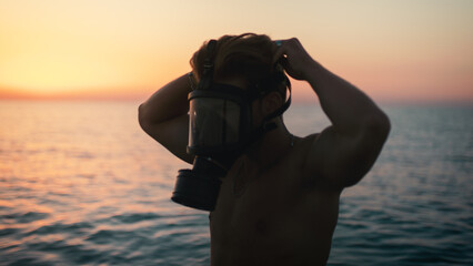 Silhouette of a boy putting on his gas mask at dawn in the ocean