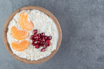 A wooden bowl of oatmeal porridge with tangerine and pomegranate