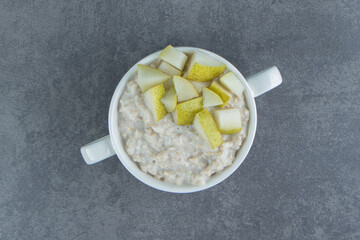 A white plate of oatmeal porridge with slices of pear