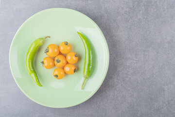 A green plate with cherry yellow tomatoes and chili peppers