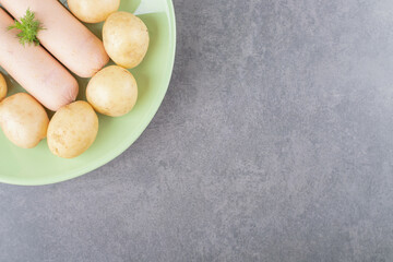 A green plate with boiled sausages and boiled potatoes