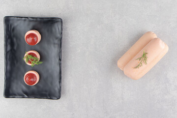 Slices of sausage with ketchup on black plate