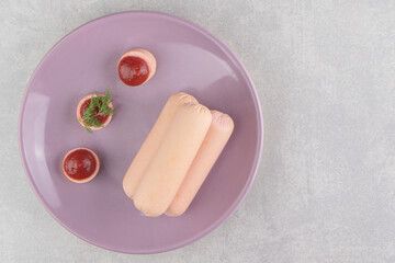 Boiled homemade sausages and ketchup on purple plate