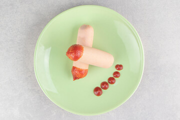 Two boiled sausages with ketchup on green plate