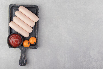Boiled sausages with ketchup and tomatoes on black board