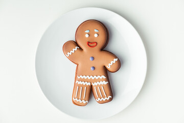 Gingerbread man with festive icing on white plate. Christmas cookie on white background. Happy New Year. Flat lay