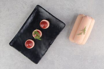 Slices of sausage with ketchup on black plate