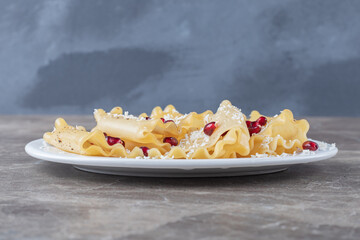 Pomegranate arils with lasagna sheets on the plate, on the marble background