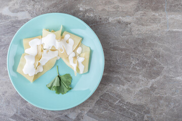 Yogurt on lasagna sheets next to greens on the plate, on the marble background
