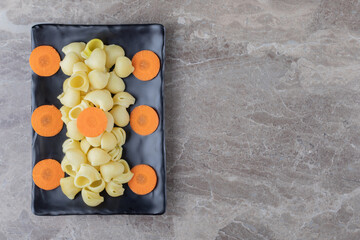 Flavorful sliced carrots next to spaghetti, on the wooden plate , on the marble background
