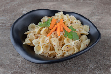 Traditional Italian pasta with finely chopped carrot and green vegetable, on the marble background