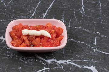 A pink plate of tomato and mayonnaise on a marble background