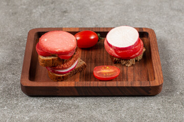 Salami sandwich and fresh tomato on wooden plate over grey background