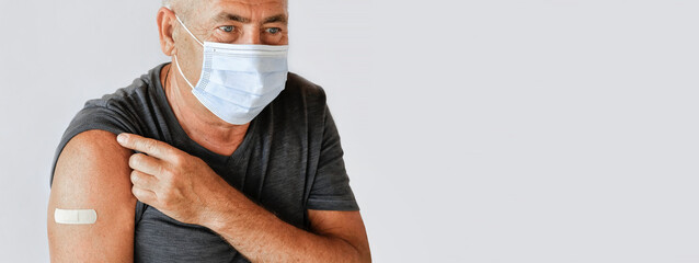 Male Senior Smiling after Receiving Vaccine. Old Man Showing Arm with Bandage, Patch after Vaccine from COVID-19 or Monkeypox. Covid, Monkey Pox Vaccination for Older People. Gray Studio Background.