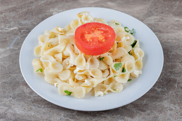 Slice tomatoes with farfalle pasta on the plate , on the marble background