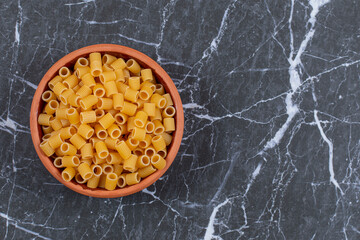 Top view raw pasta penne on wooden bowl