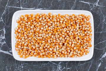 Pile of fresh corn seeds on white plate over black background