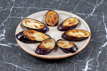 Fried fresh aubergine (eggplant) slices on white plate over black background
