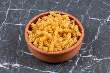 Raw pasta penne in pottery bowl over stone background