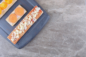 Sliced carrots, cheese and tomatoes on crispy breads on the wooden tray, on the marble background