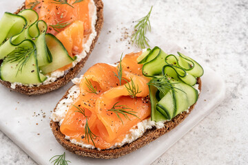 Rye bread open sandwiches with salted salmon and cucumber on a white stone table. Healthy food.