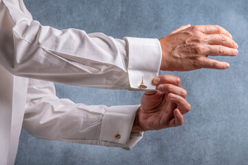 A man buttons his white shirt with gold cufflinks