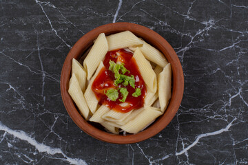 Close up photo of boiled penne pasta with ketchup sauce in pottery bowl