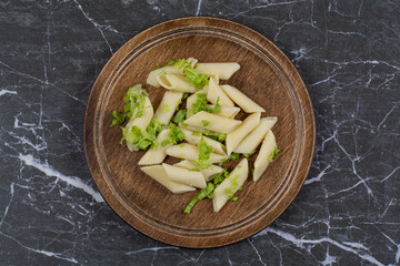 Top view of penne pasta with greens on wooden board