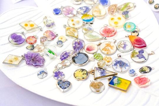 Epoxy Resin Jewelry - Many Handmade Pendants With Real Flowers And Plants Inside On White Stand. Making Exclusive Jewellery At Home